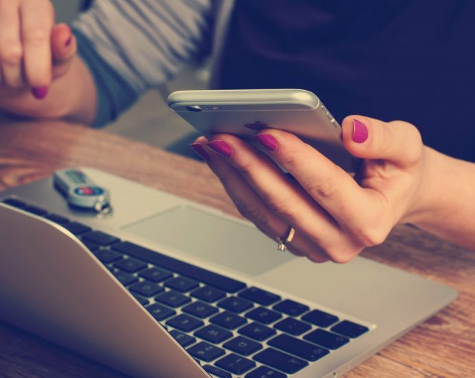 person sat at laptop with phone in hand too.