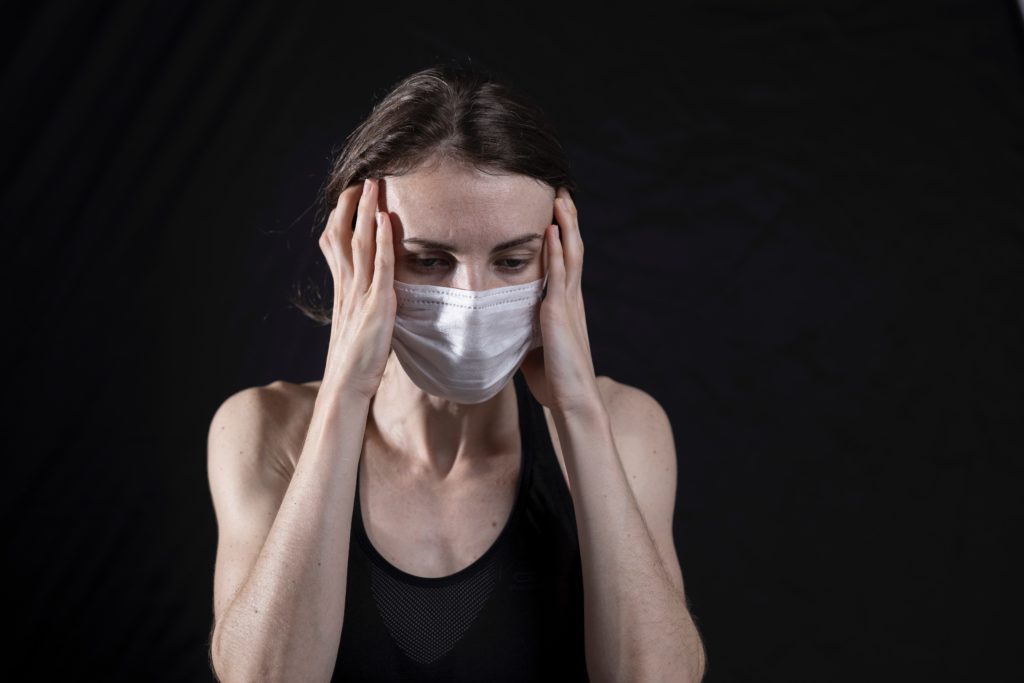 Young woman wearing a coronavirus mask with her hands on her temples.