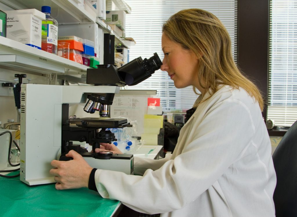 Female cancer researcher looking at a sample under a microscope