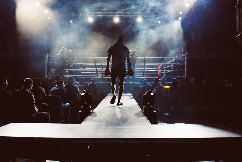 Man walking towards a boxing ring surrounded by crowd