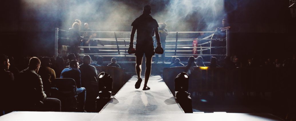 Man walking towards a boxing ring surrounded by crowd