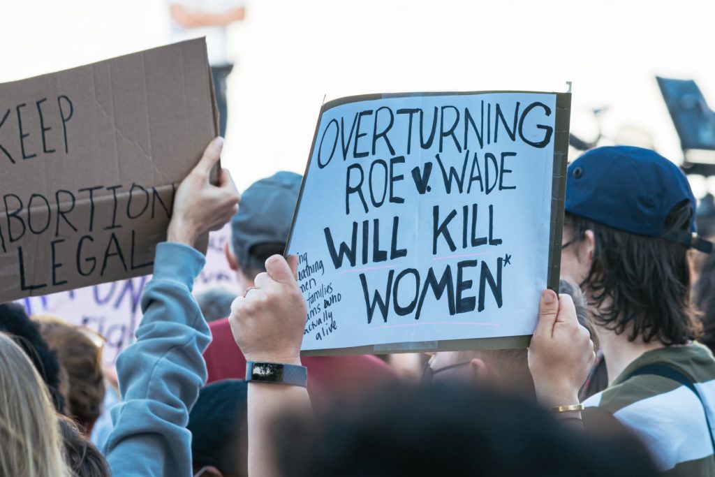 White sign with black writing held at a protest saying "overturning Roe v Wade will kill women" and another one saying keep abortion legal