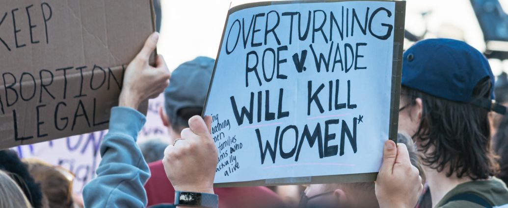 White sign with black writing held at a protest saying "overturning Roe v Wade will kill women" and another one saying keep abortion legal