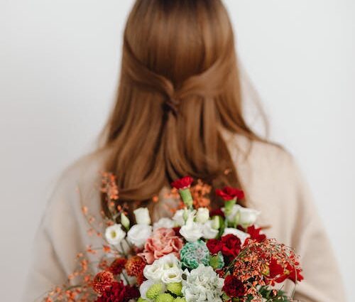 Red headed woman with her back to the camera, holding a bouquet of flowers behind her. She likens the main character of It Ends With Us.