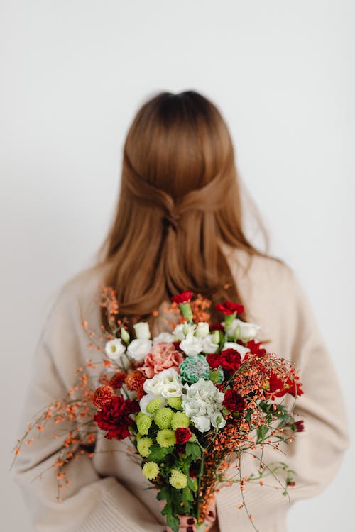 Red headed woman with her back to the camera, holding a bouquet of flowers behind her. She likens the main character of It Ends With Us.