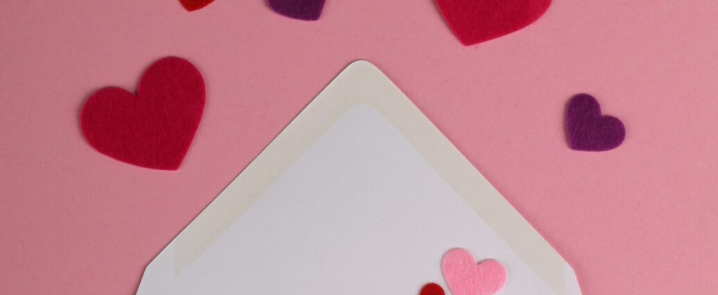 An open white envelope laid flat against a pink background. Emerging from the envelope are some carefully-cut pink and purple paper hearts. The image is used to reflect the love and emotion that Sabrina Carpenter put into her album, based on emails she sent to herself.