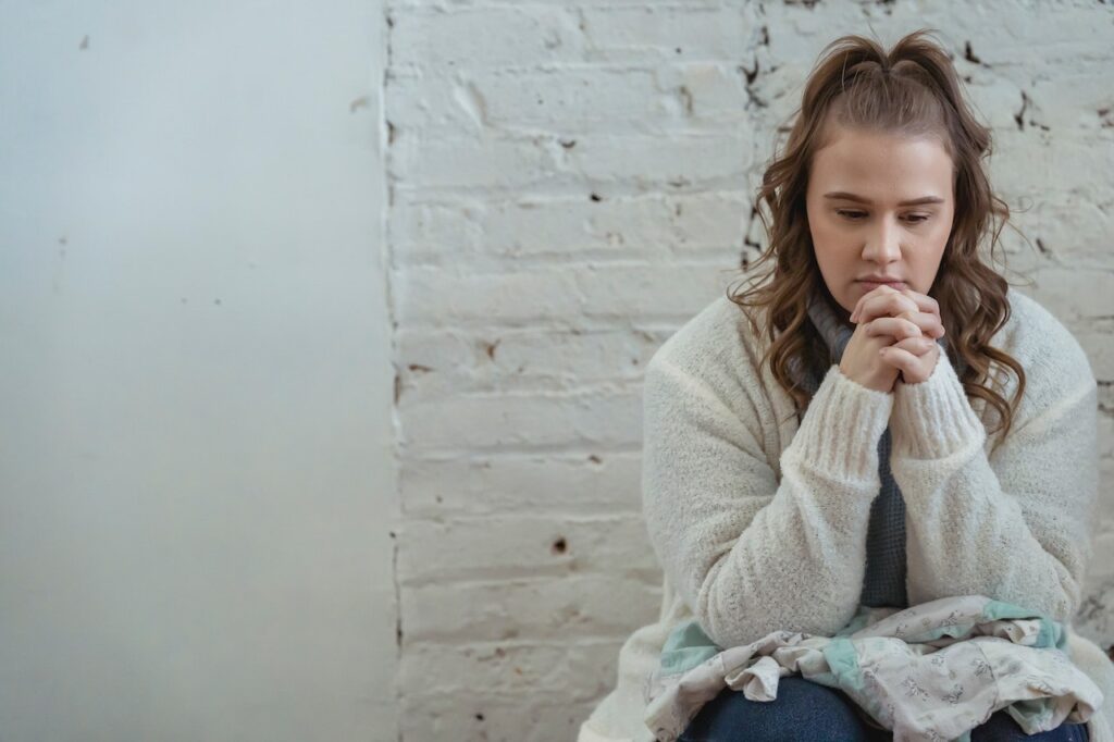 Upset woman wearing white cardigan with fingers clasped, thinking about next steps