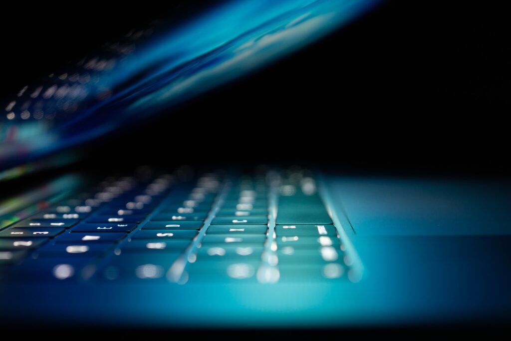 Side view of a laptop folded almost completely down. The room is dark so the only light is a blue-green glow from the screen. It sets the sinister tone of the story about Stephen Bear's crimes.