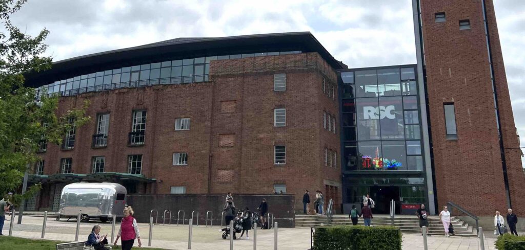 Entrance to a theatre in daylight with a tower to the right and a few people passing by