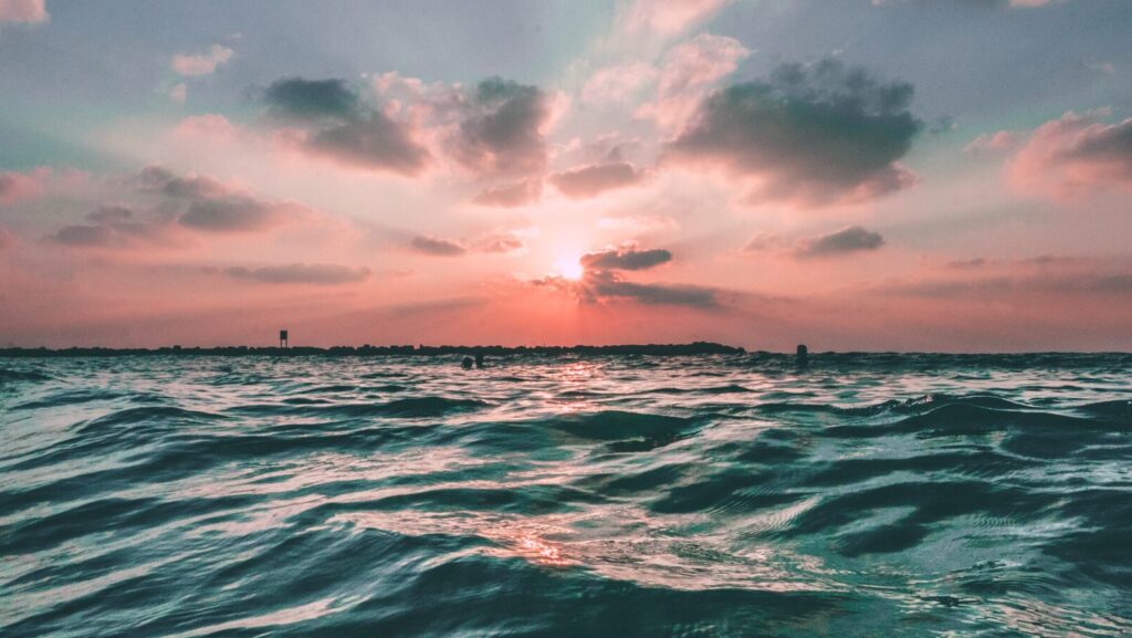 A blue ocean with calm waves underneath a candyfloss pink sunset