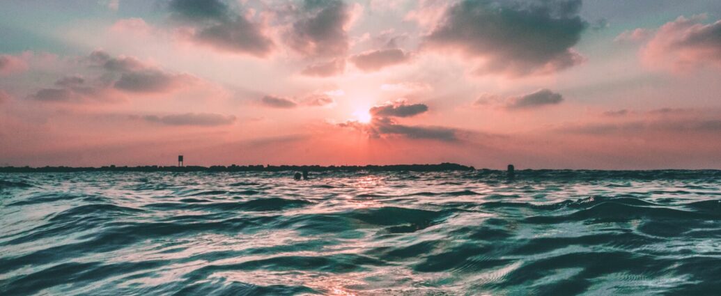 A blue ocean with calm waves underneath a candyfloss pink sunset