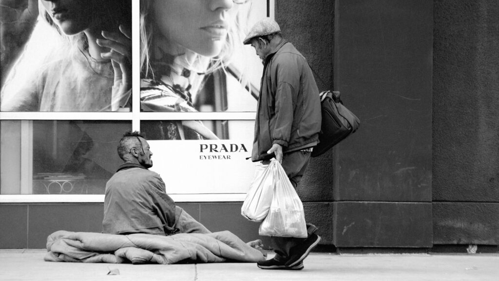 A homeless man sitting outside a Prada fashion store.