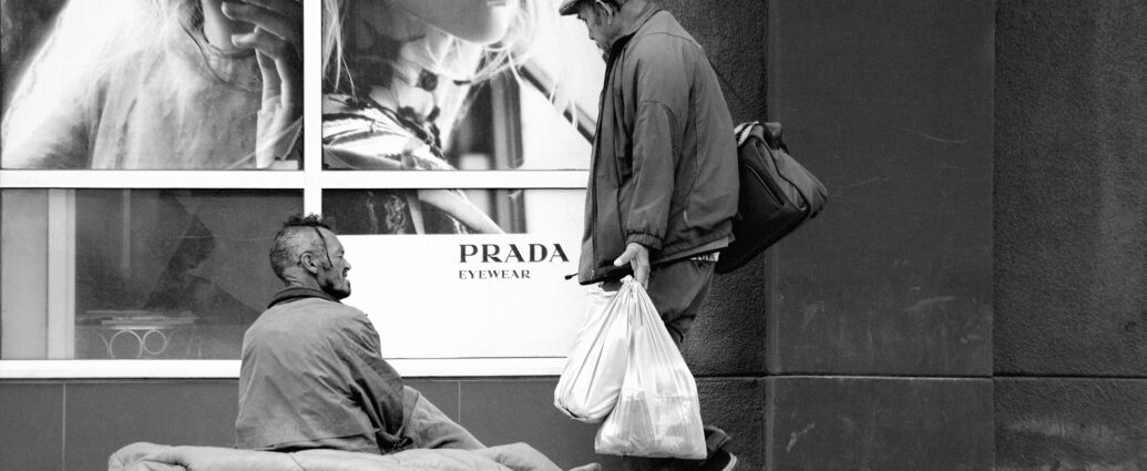 A homeless man sitting outside a Prada fashion store.