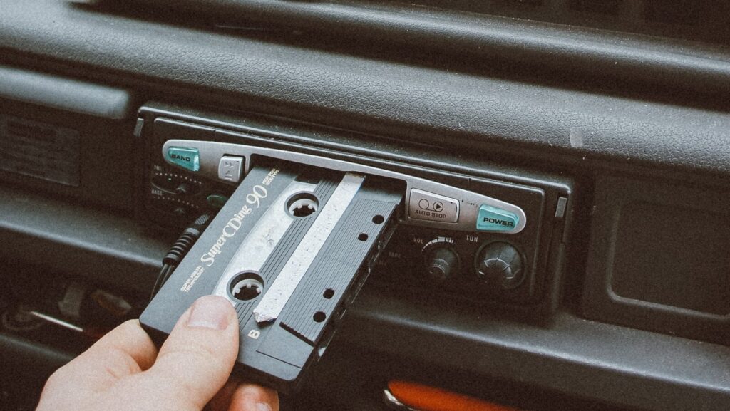 A vintage style shot of somebody inserting a cassette into the cassette player of their car.