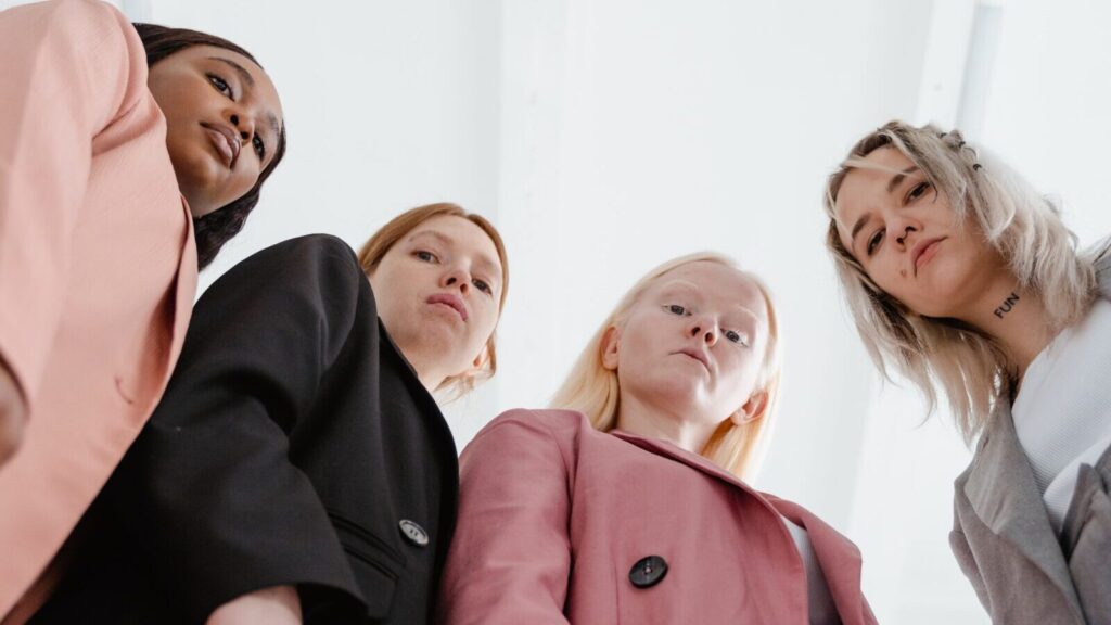 Image shows four women with stern expressions looking down towards the camera