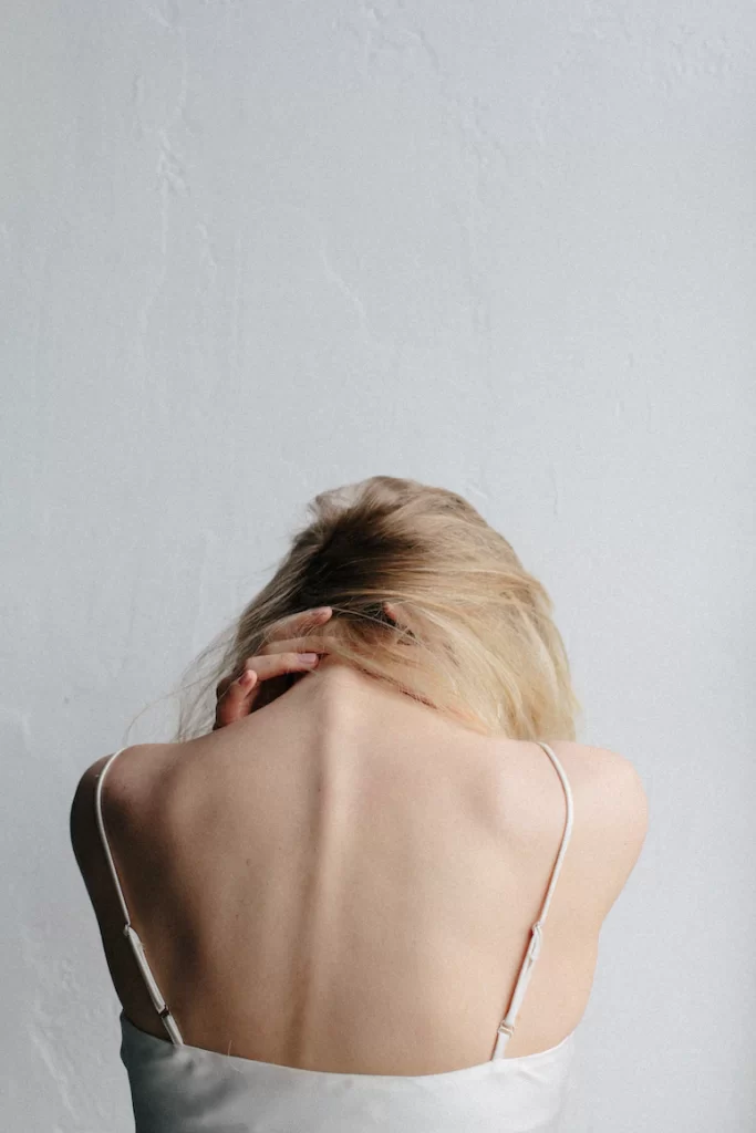 A young white woman in blonde hair gripping her neck in distress.