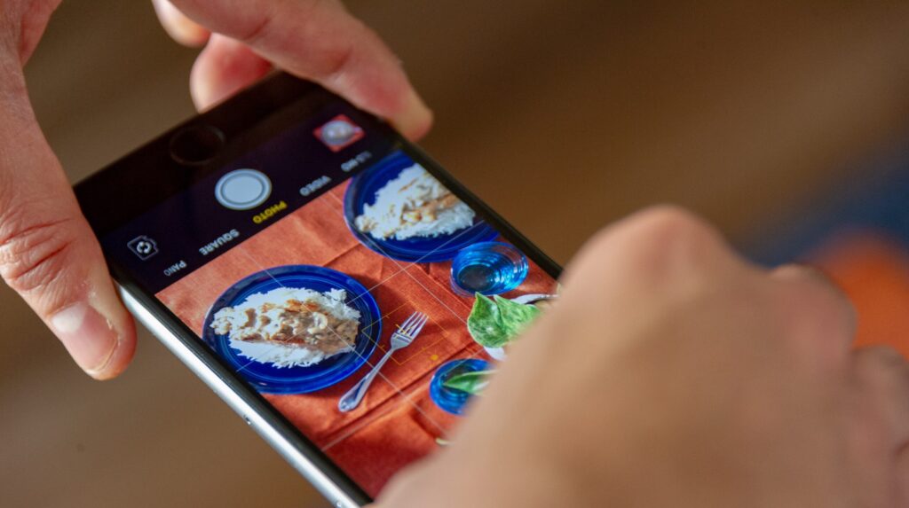 Two hands holding an iPhone, taking a picture of food.