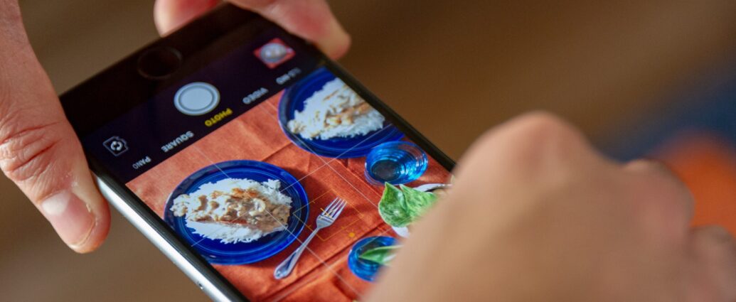 Two hands holding an iPhone, taking a picture of food.