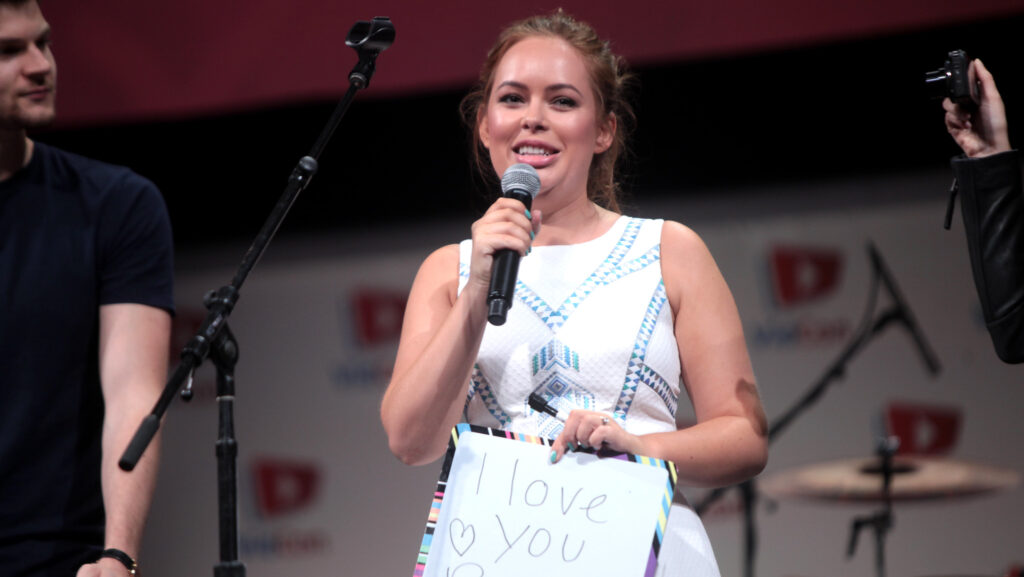 Tanya Burr speaking at the 2014 VidCon. She holds a sign that reads 'I love you Burr bears'.