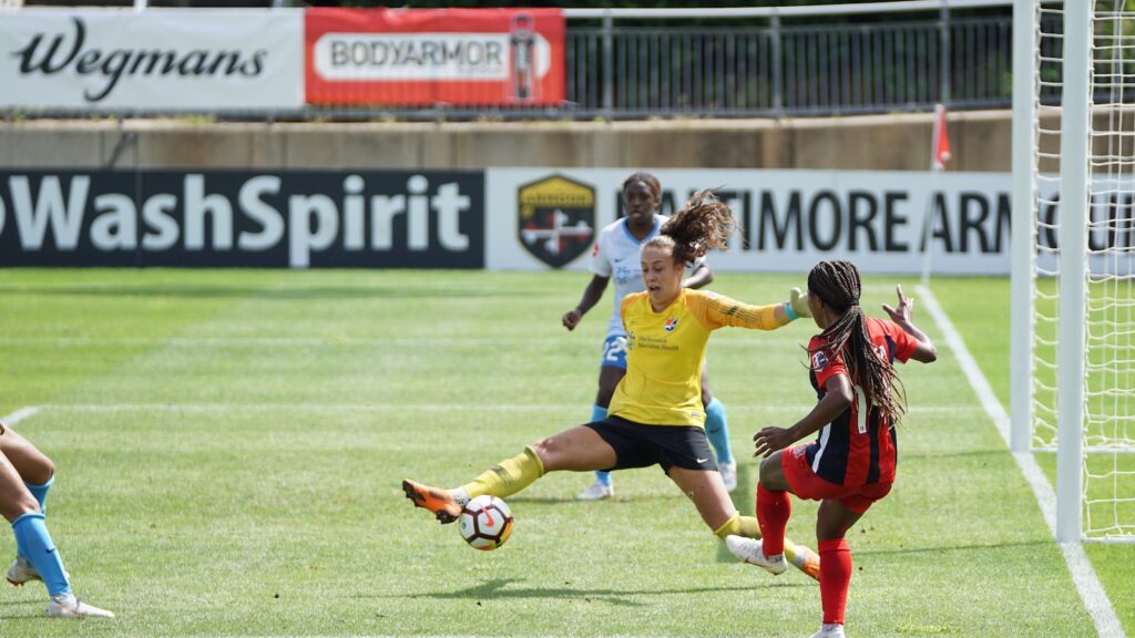 Female footballers playing football near a goal.