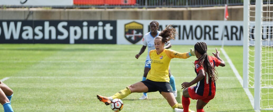 Female footballers playing football near a goal.