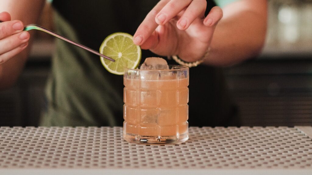 Image shows a bartender placing a lime on the rim of a non-alcoholic cocktail