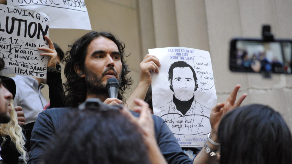 Image shows Russell Brand speaking at a protest on Wall Street, NYC.