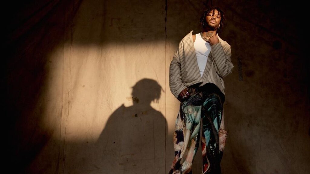 Singer VJ Jaxson stands onstage with a curtain and a shadow behind him.