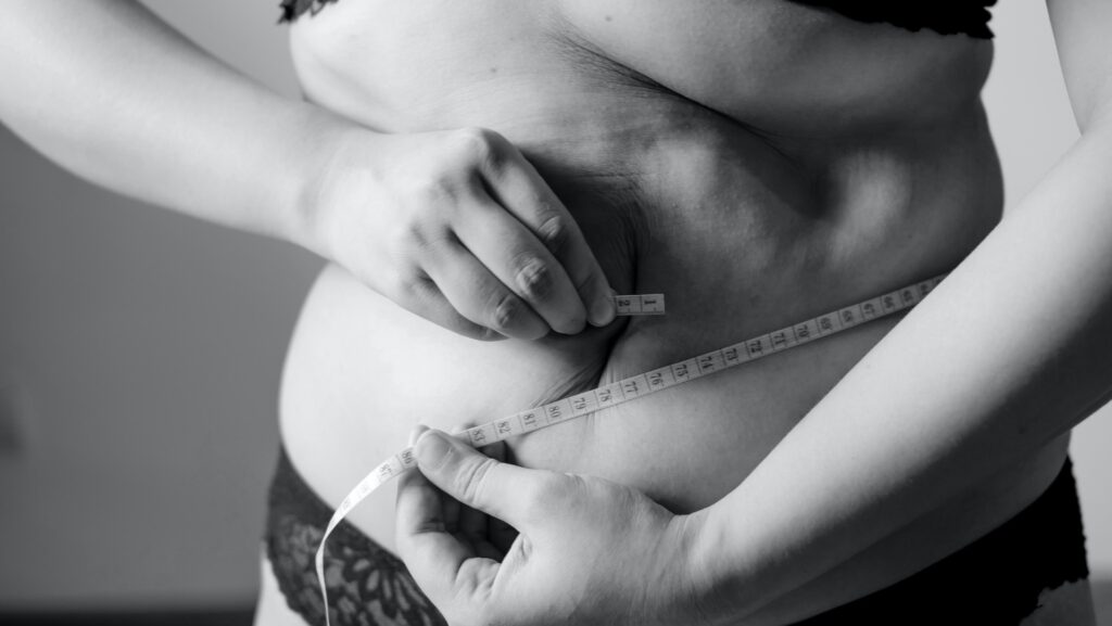 Grayscale photo of woman wrapping measuring tape around her stomach.