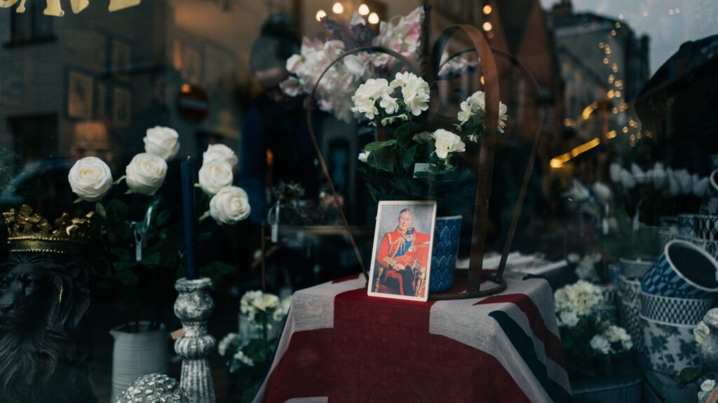 Displays a framed photo of Charles III in a shop window.