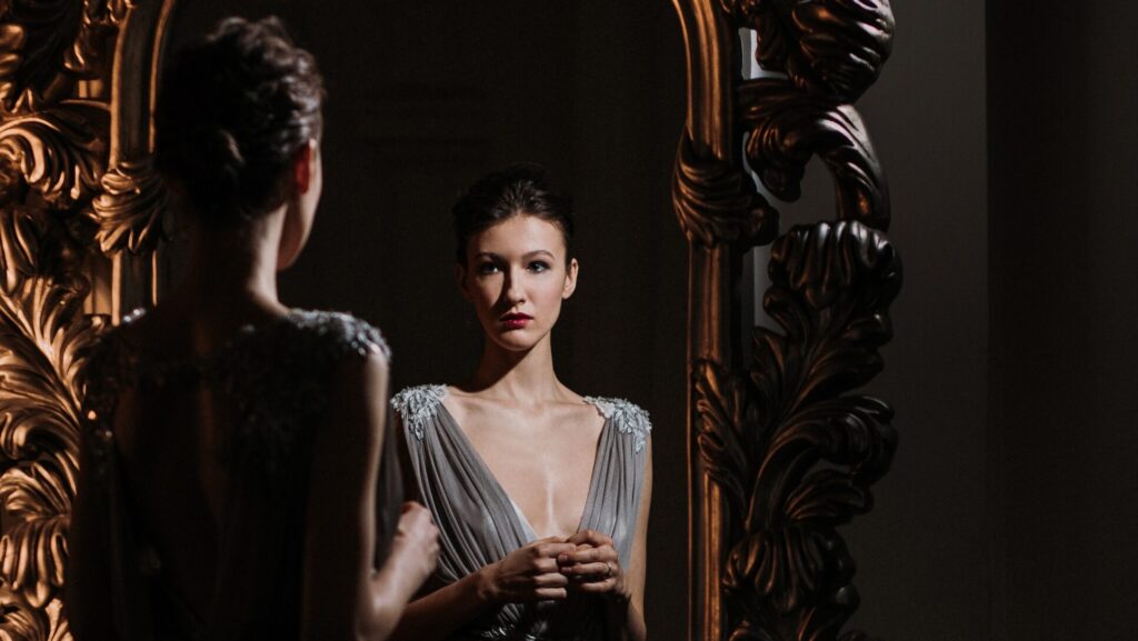 Brunette woman dressed in silver dress looking in mirror.