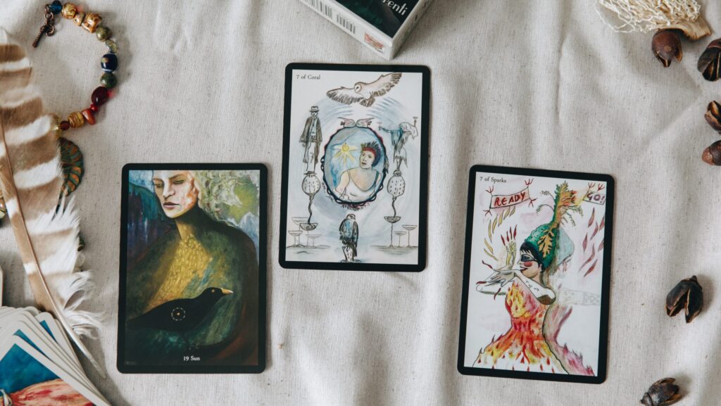 Image shows three tarot cards facing upwards on a table, surrounded by feathers and beads [Why do men hate astrology?]