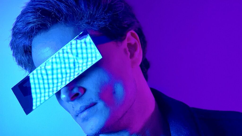 A man in a jacket wears some shades in a purple room.