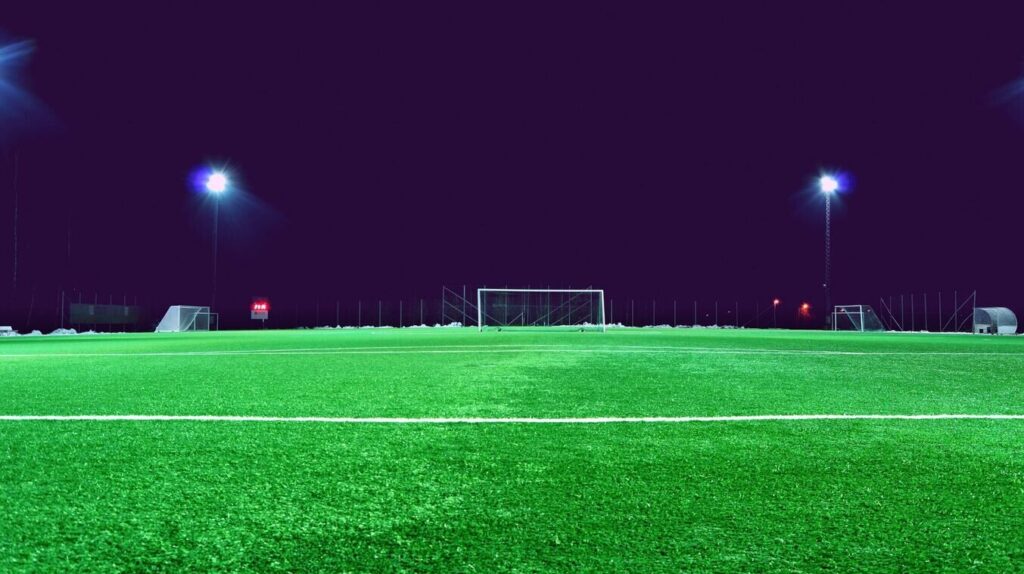 Football net and green grass of football field with dark sky lit by flood lights. Expensive Transfers.