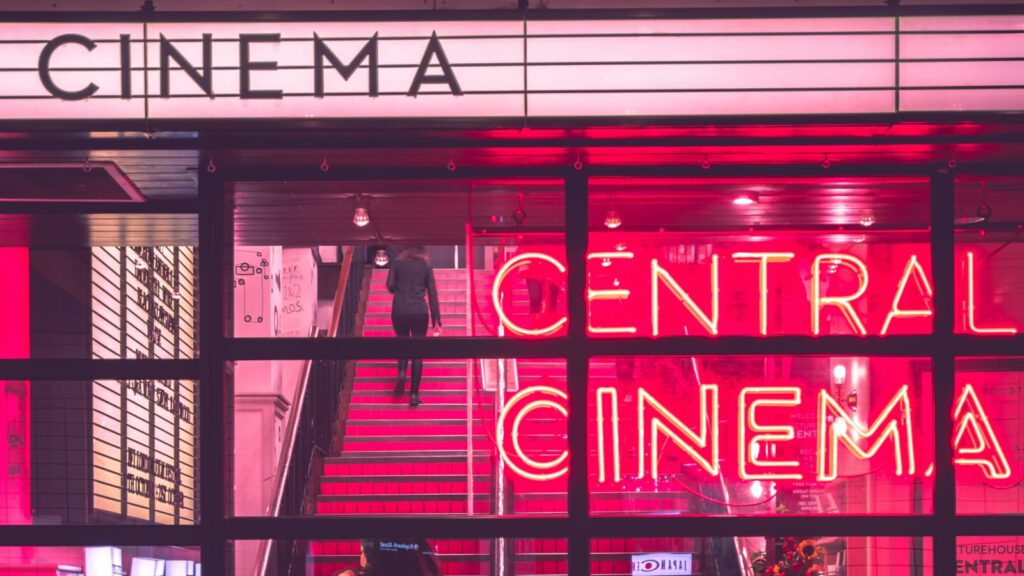 The exterior of a retro-style cinema with neon pink signs.