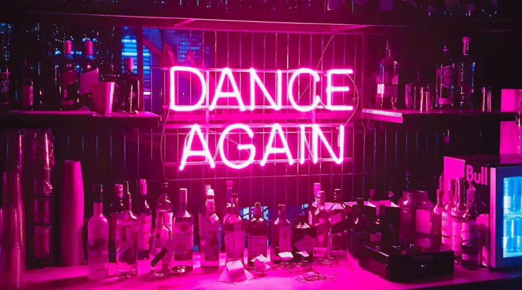 Neon light sign reading DANCE AGAIN in a bar.