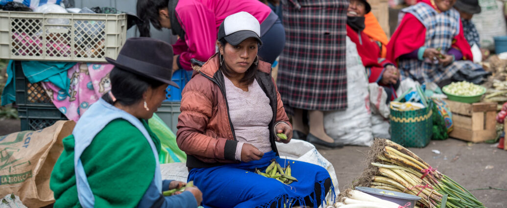 Two women sat behind a pile of vegetables on a busy market street in Ecuador.