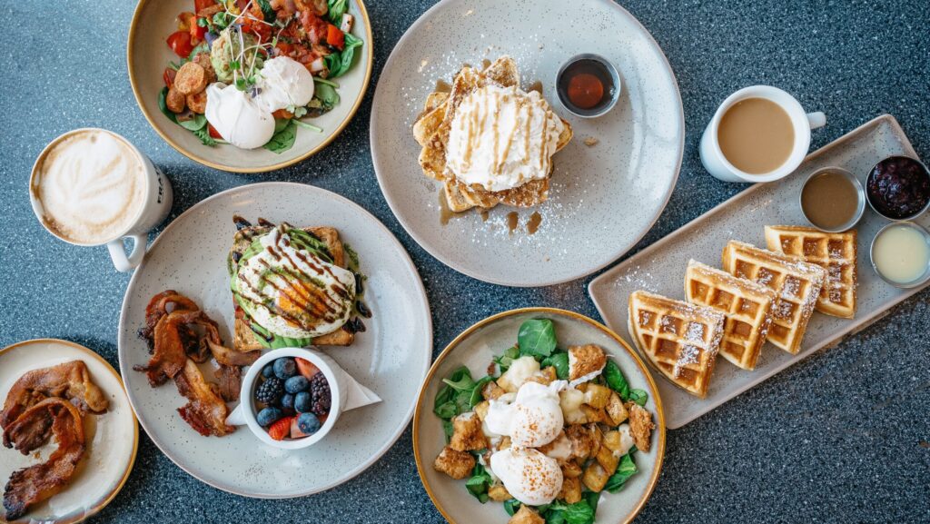 A table of brunch dishes including eggs on toast, bacon, berries and waffles.