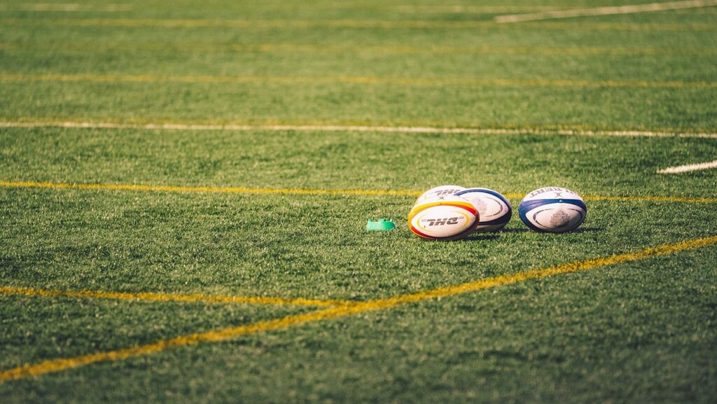 Image shows three rugby balls on a pitch.