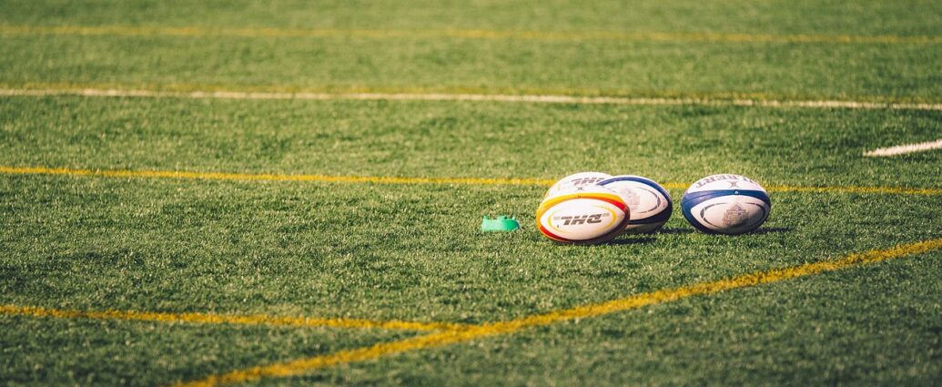 Image shows three rugby balls on a pitch.