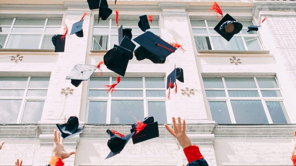 Image shows a group of graduates throwing their caps into the air [after graduating]