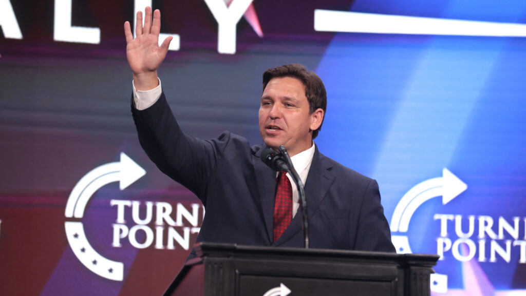 Ron DeSantis raises his arm while speaking at a podium.