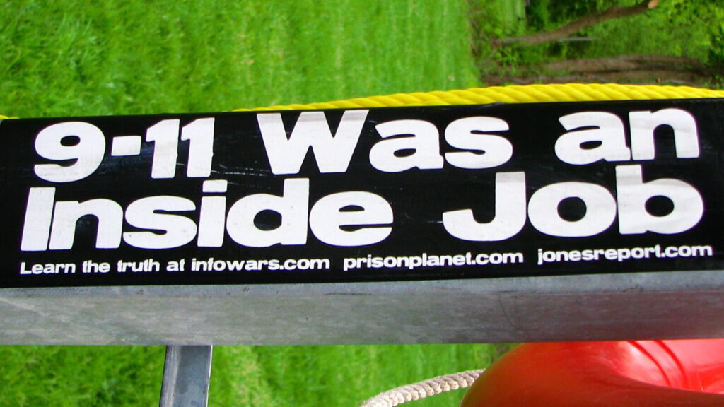 Image shows a sticker that reads '9/11 was an inside job' [conspiracy theories]