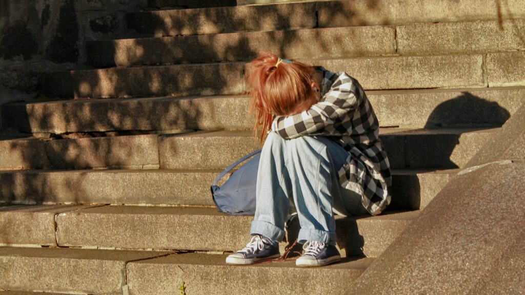 Image shows a young girl crying into her knees [children's mental health crisis]