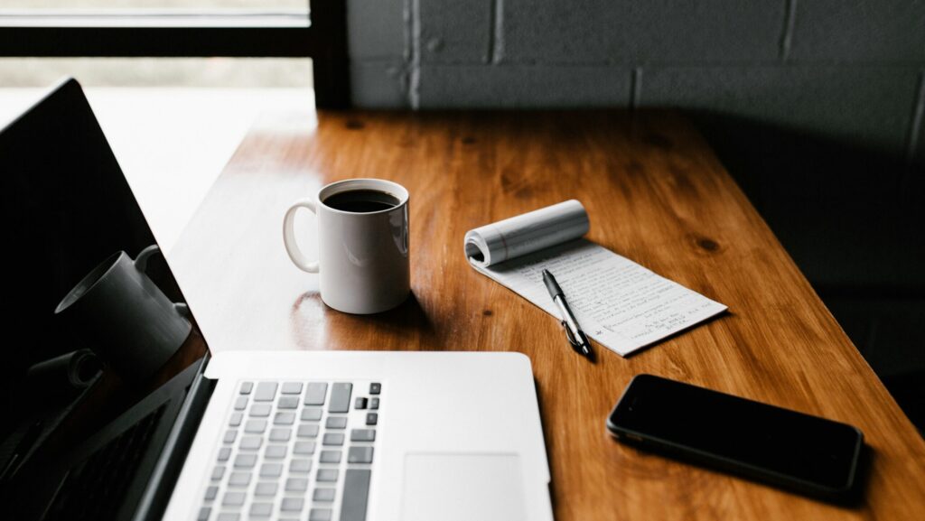 Desk with laptop, phone, coffee and notepad.