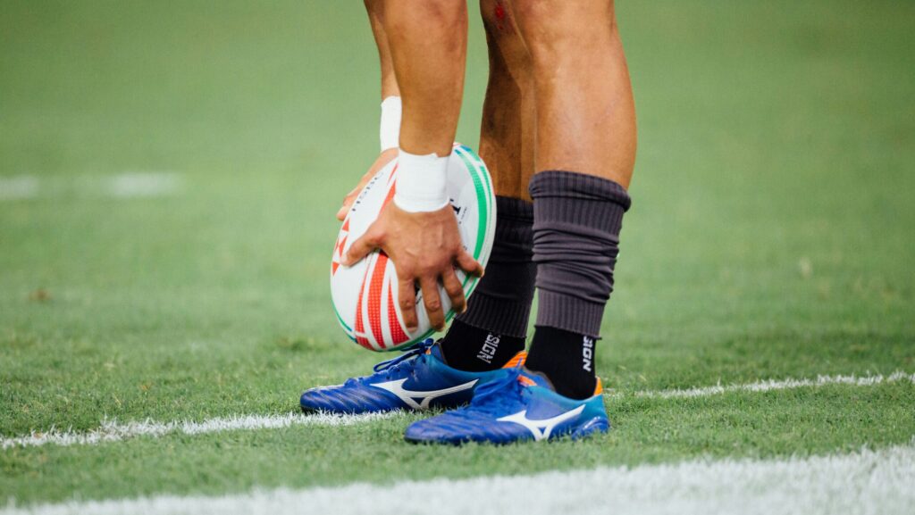 Scotland England. man wearing blue rugby boots holding rugby ball above togs.