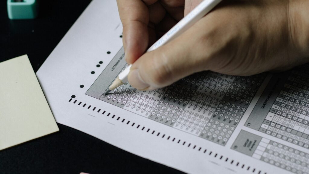 Image shows a hand filling in a multiple choice exam paper [English test scandal].