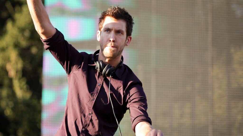 Calvin Harris doing a DJ set at a festival with one hand up in the air, 2012.