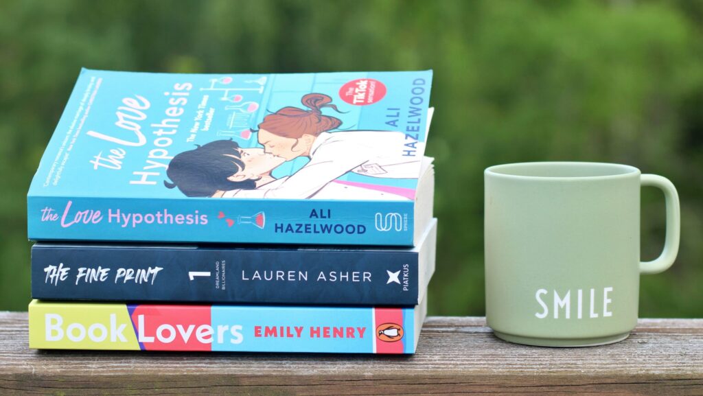 Three love stories on a shelf next to a coffee mug backed by greenery.