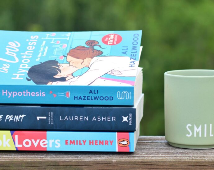 Three love stories on a shelf next to a coffee mug backed by greenery.